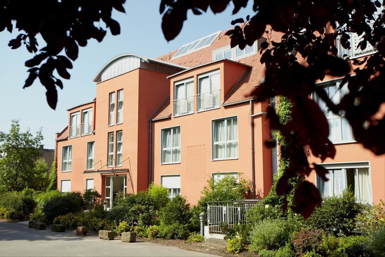 A multi-story building with a curved roof, large windows, and a well-maintained garden.