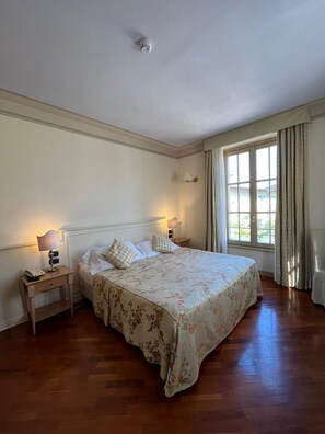 Een slaapkamer met een groot bed, twee nachtkastjes met lampen, een rookmelder in het plafond en een raam met gordijnen.