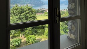Ein Zimmer mit großem Fenster und Blick auf einen See, Berge und grüne Landschaft.
