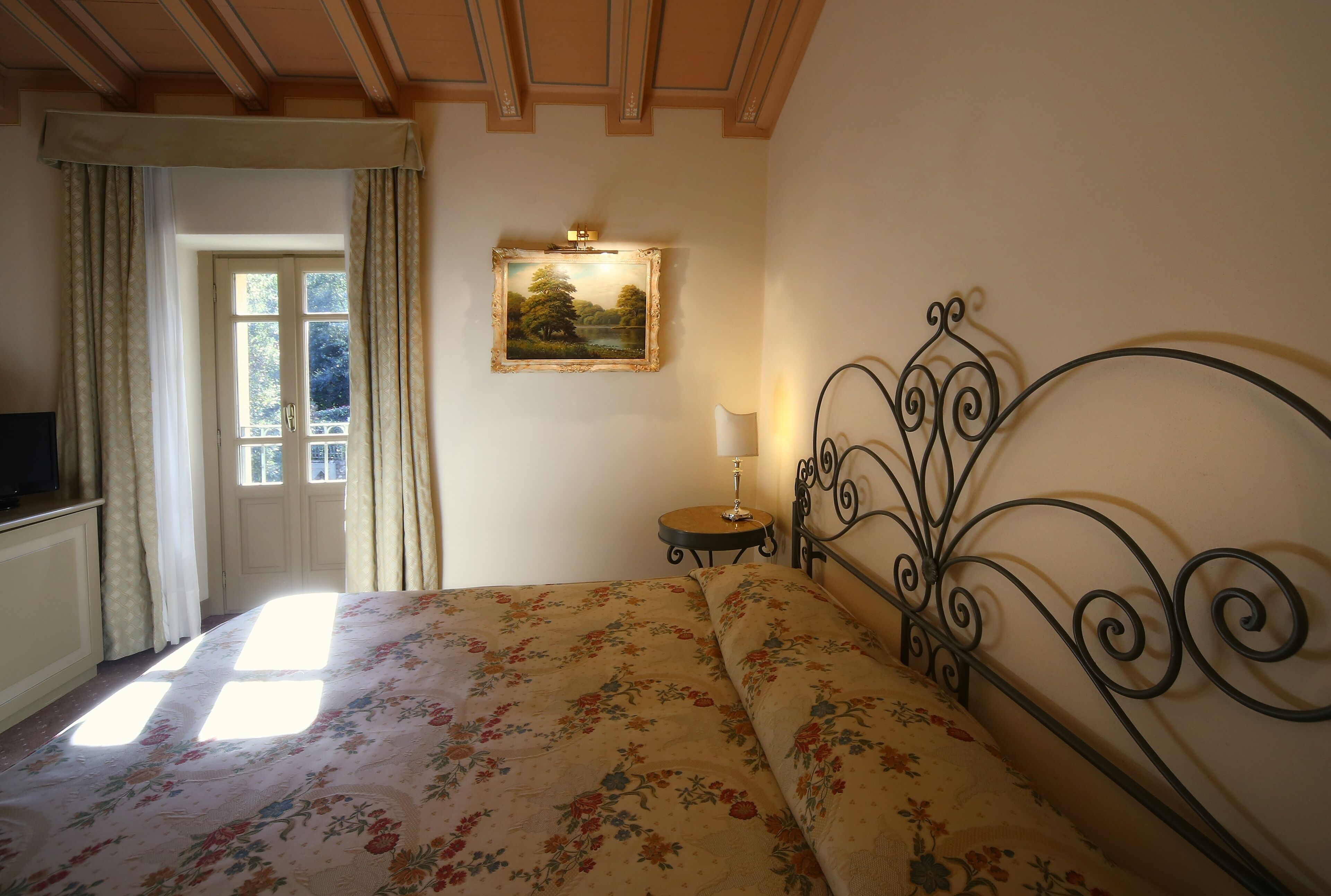 A bedroom with a bed, a bedside table with a lamp, a framed picture on the wall, and a window with curtains.