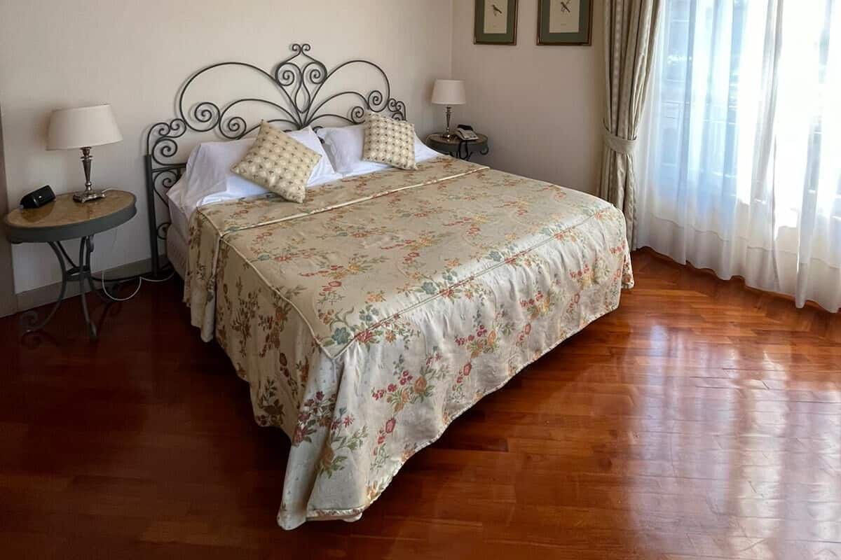 Ein ordentlich eingerichtetes Schlafzimmer mit Bett, Nachttischen und einem Fenster mit Vorhängen.