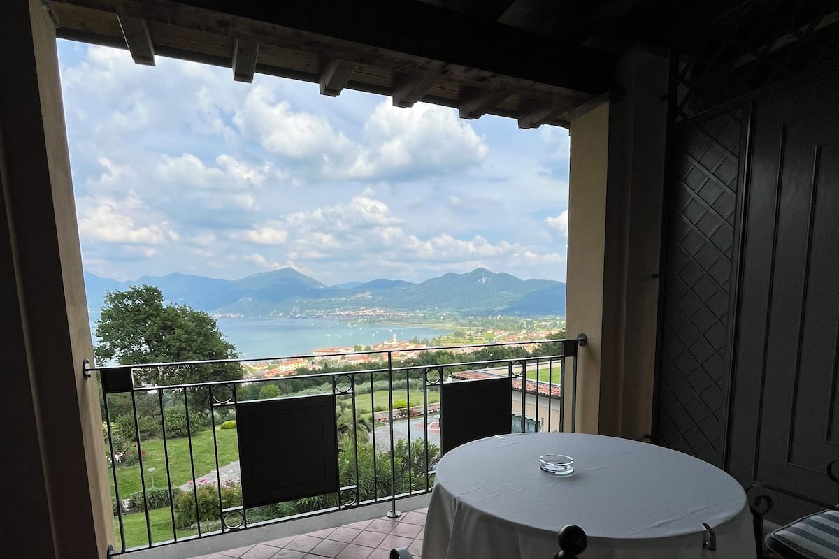 Ein Balkon mit Tisch und Stühlen, mit Blick auf eine malerische Landschaft mit Bergen und einem Gewässer.