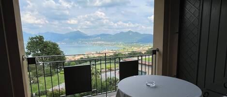 Un balcon avec une table et des chaises, donnant sur un paysage pittoresque avec des montagnes et une étendue d’eau.