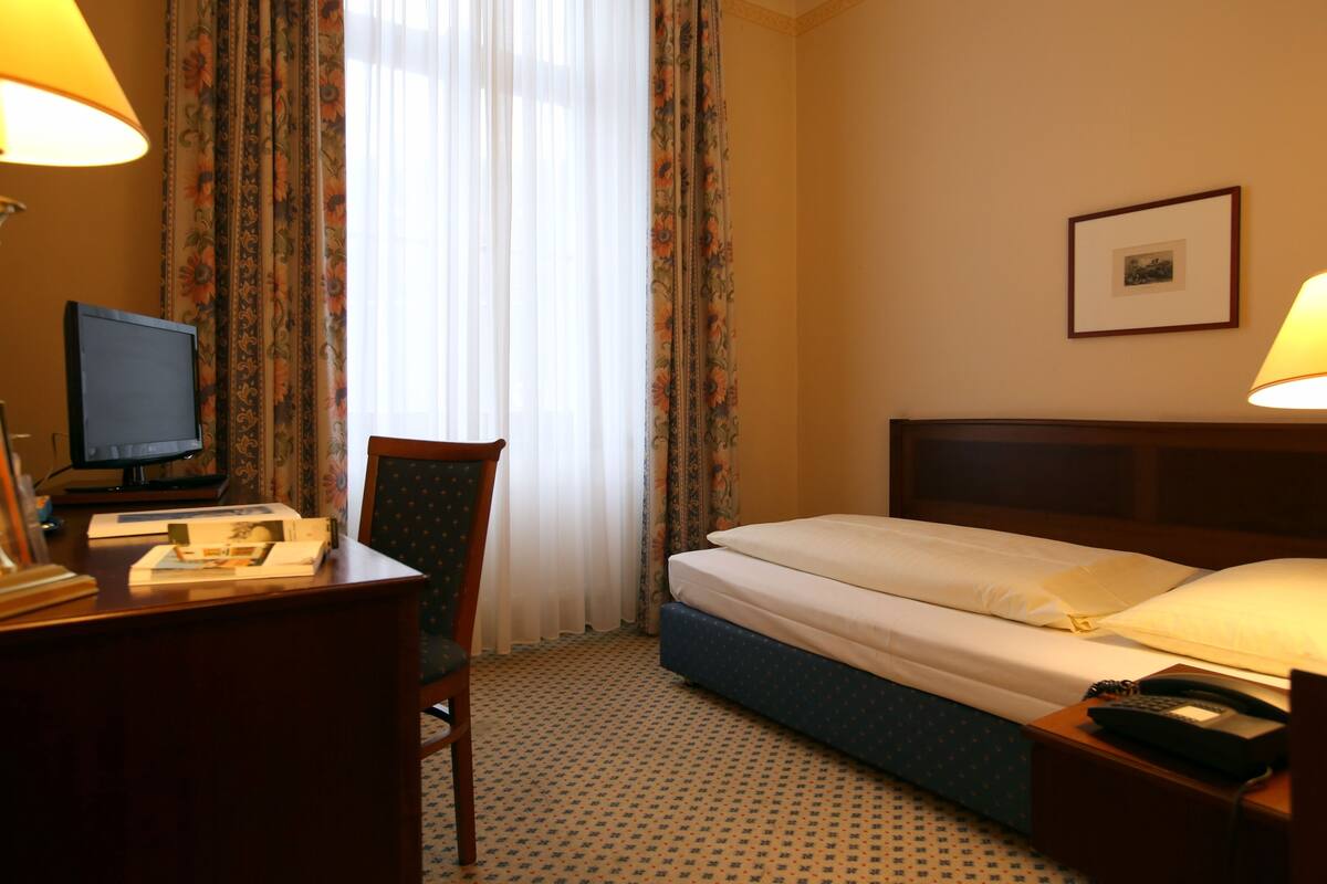 Habitación de hotel con cama, escritorio con computadora, silla, teléfono y un cuadro en la pared.