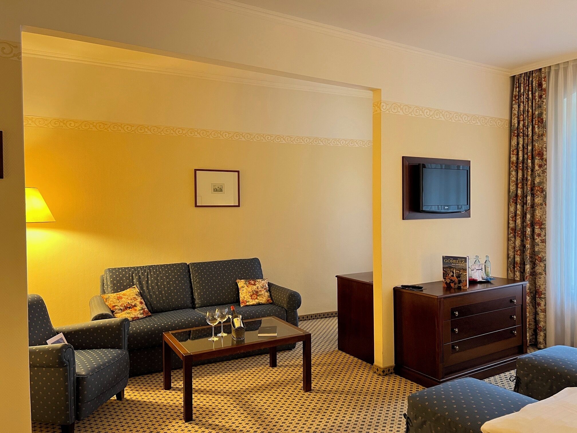 A hotel room with a sofa, a coffee table, a TV, a dresser, and a patterned carpet.