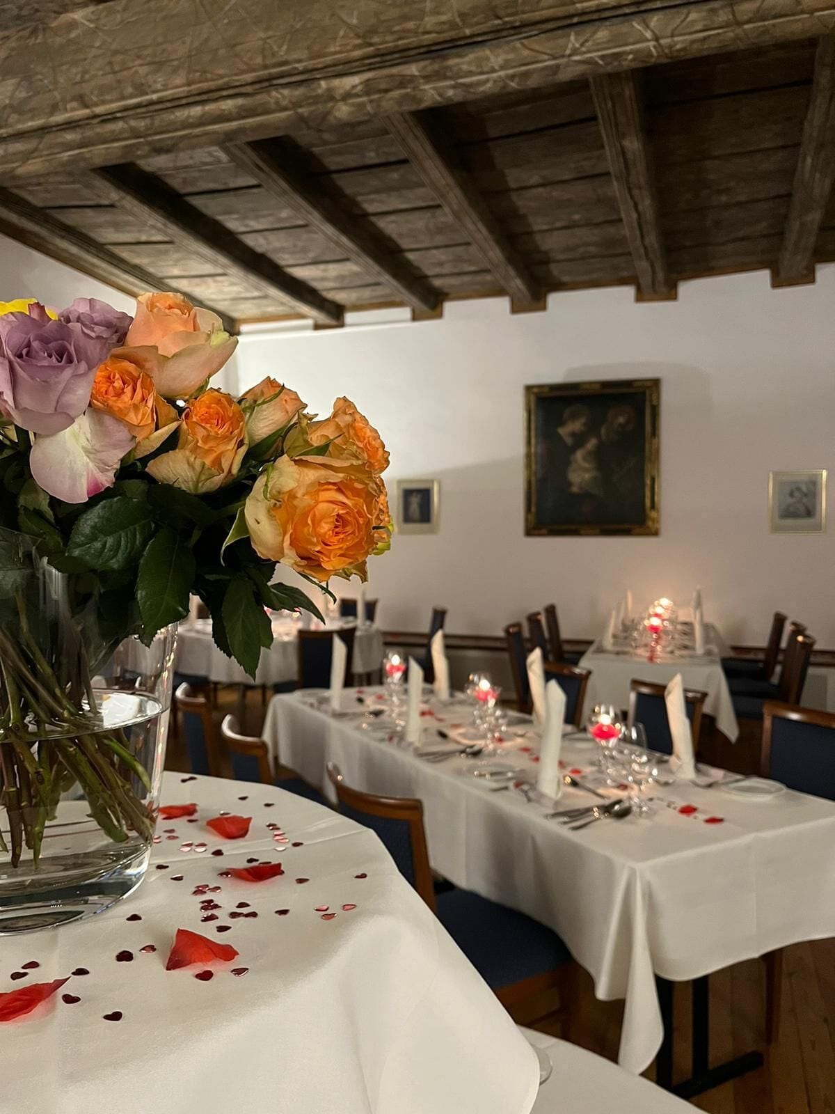 A dining area with tables set for a meal, a vase of flowers on the table, and a painting on the wall.