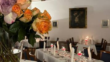 A dining area with tables set for a meal, a vase of flowers on the table, and a painting on the wall.