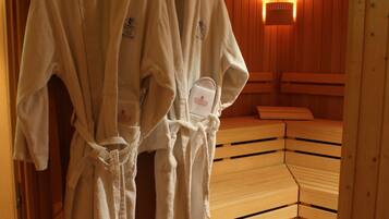A sauna room with wooden benches and two white robes hanging on a rack.