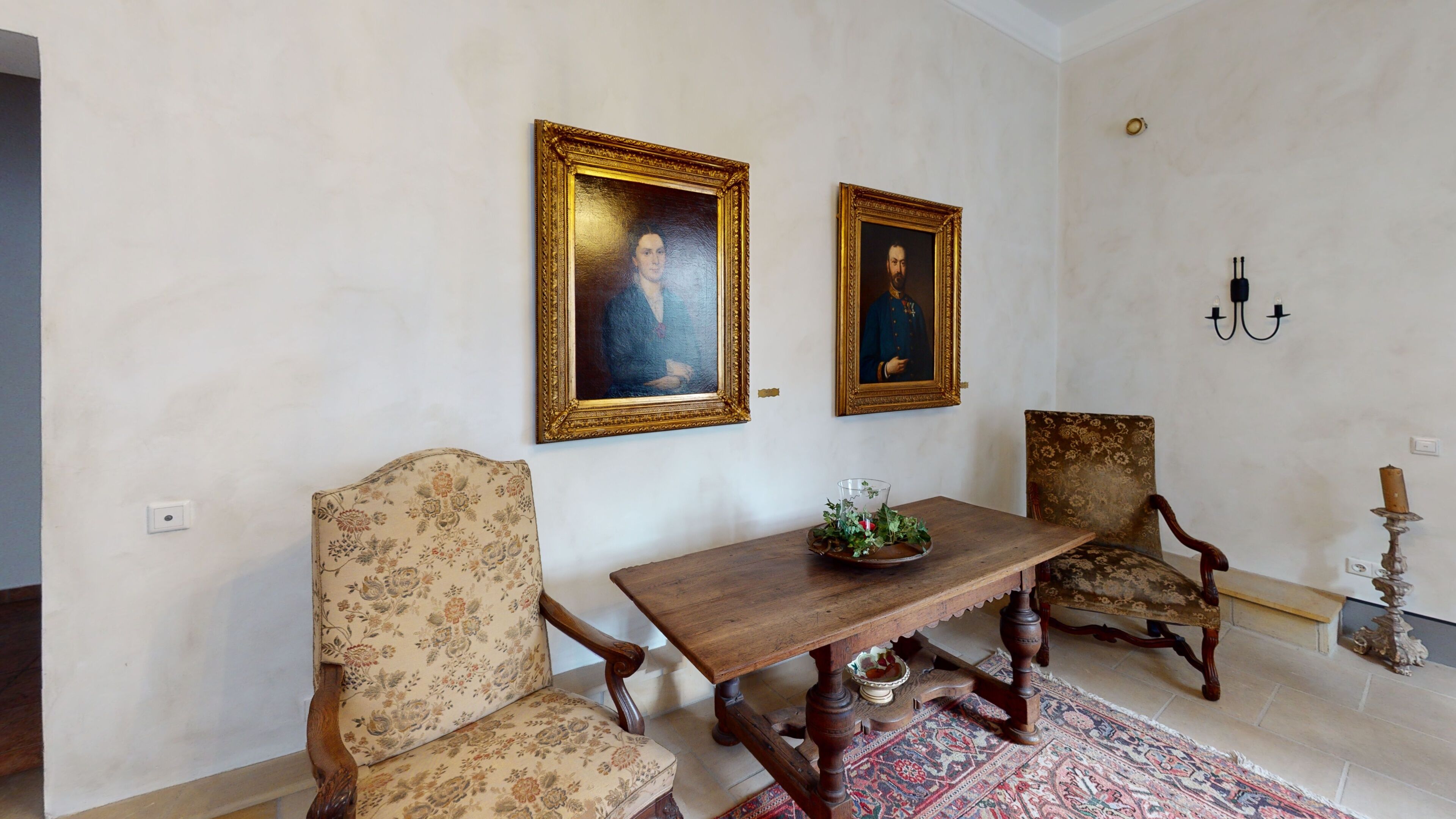 Una stanza con un tavolo in legno, due poltrone imbottite e due quadri appesi al muro.