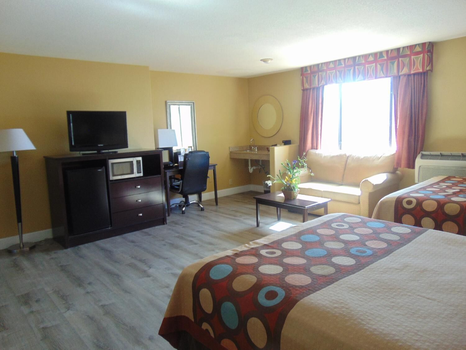 A hotel room with a bed, a desk, a TV, a chair, a sofa, and a window with curtains.