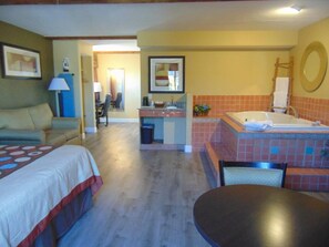 A hotel room with a bed, a desk, a chair, a small table, a bathroom with a bathtub, and a mirror. - Super 8 by Wyndham Payson (Payson)