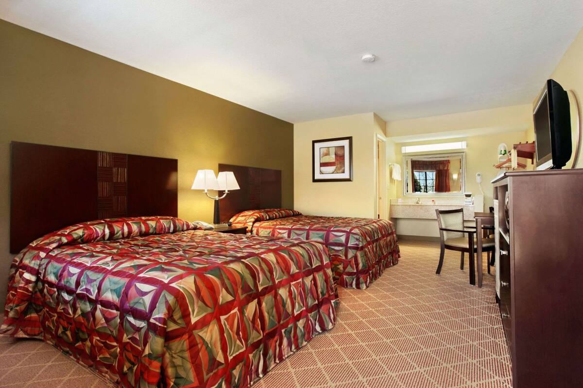 A hotel room with two beds, a desk, a chair, a mirror, and a television.