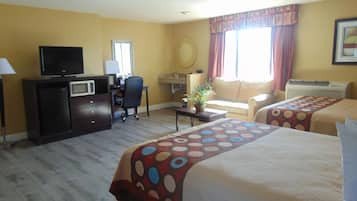 A hotel room with two beds, a desk with a computer, a television, and a small kitchenette.
