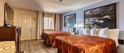 A hotel room with two beds, a desk, a chair, a mirror, a door, and a window.