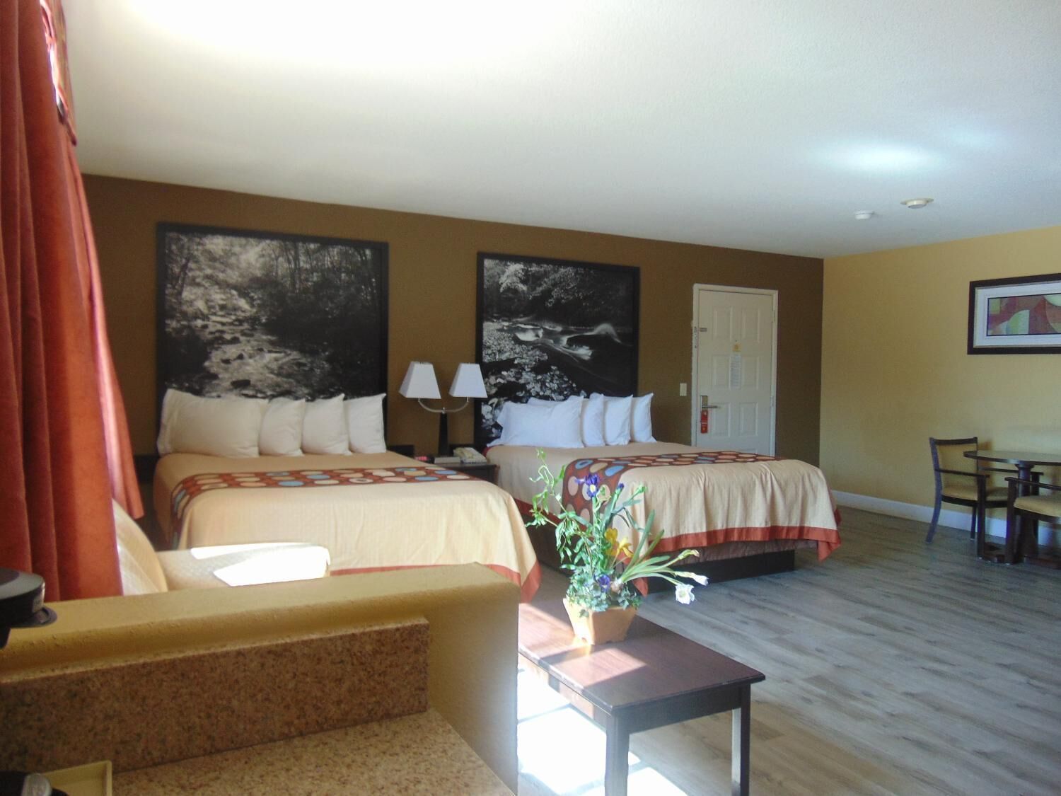 A hotel room with two beds, a desk, a chair, and a potted plant.