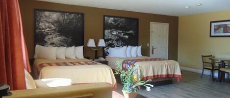 A hotel room with two beds, a desk, a chair, and a potted plant.