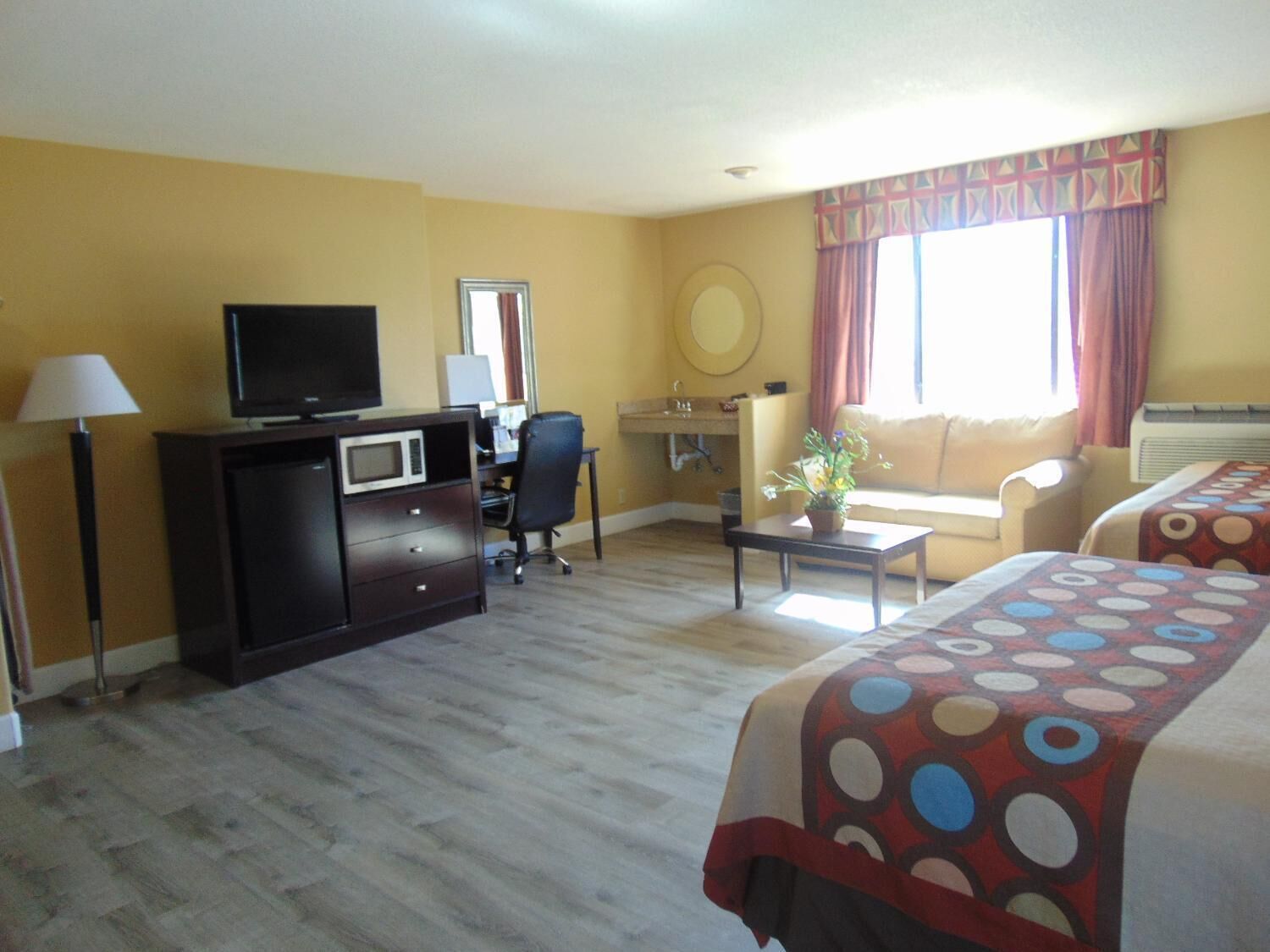 Habitación de hotel con televisión, escritorio, silla, dos camas, una mesita con una planta y ventana con cortinas.