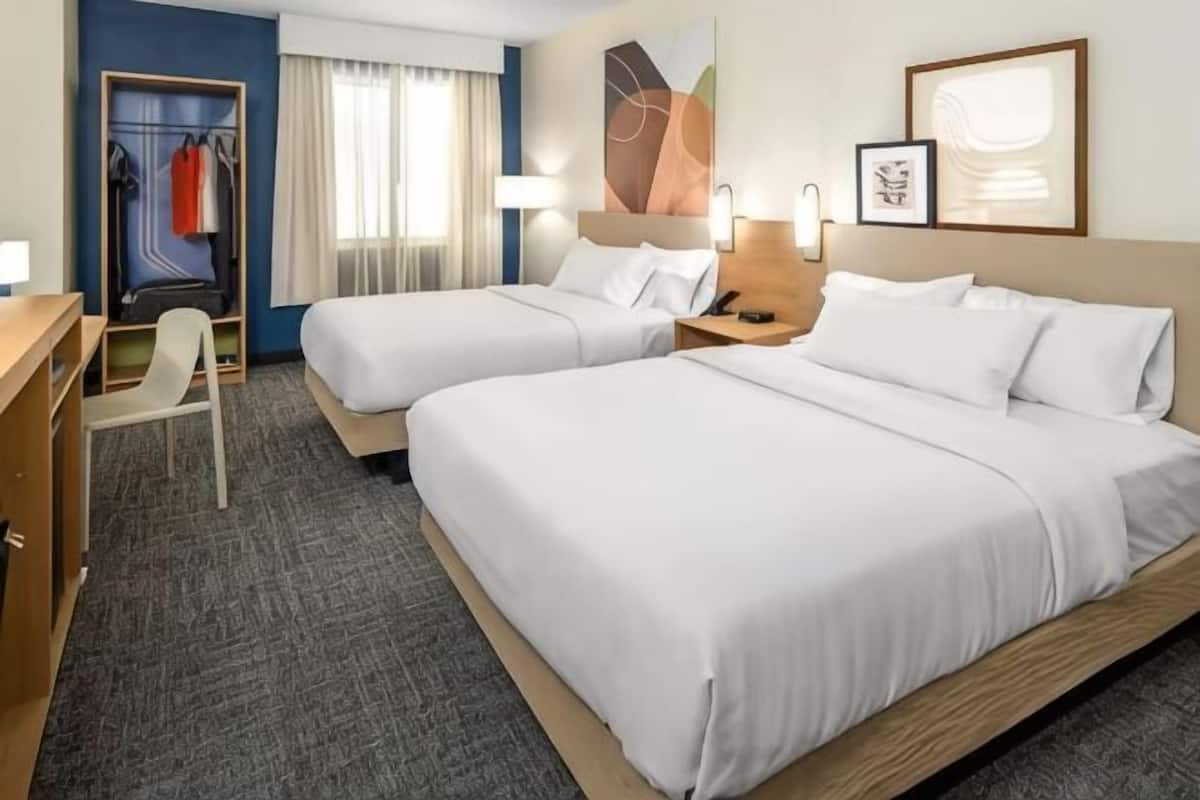 A hotel room with two beds, a desk, a chair, a wardrobe, and a window with curtains.