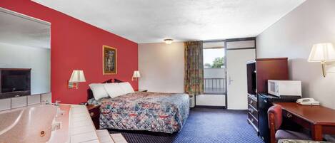 Ein Hotelzimmer mit einem großen Bett, einem separaten Badezimmer mit Badewanne, einem Schreibtisch mit Stuhl und einem Fernseher.