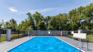 A rectangular swimming pool with clear blue water, surrounded by a black metal fence, and benches along the edge. - Days Inn by Wyndham Martin (Martin)