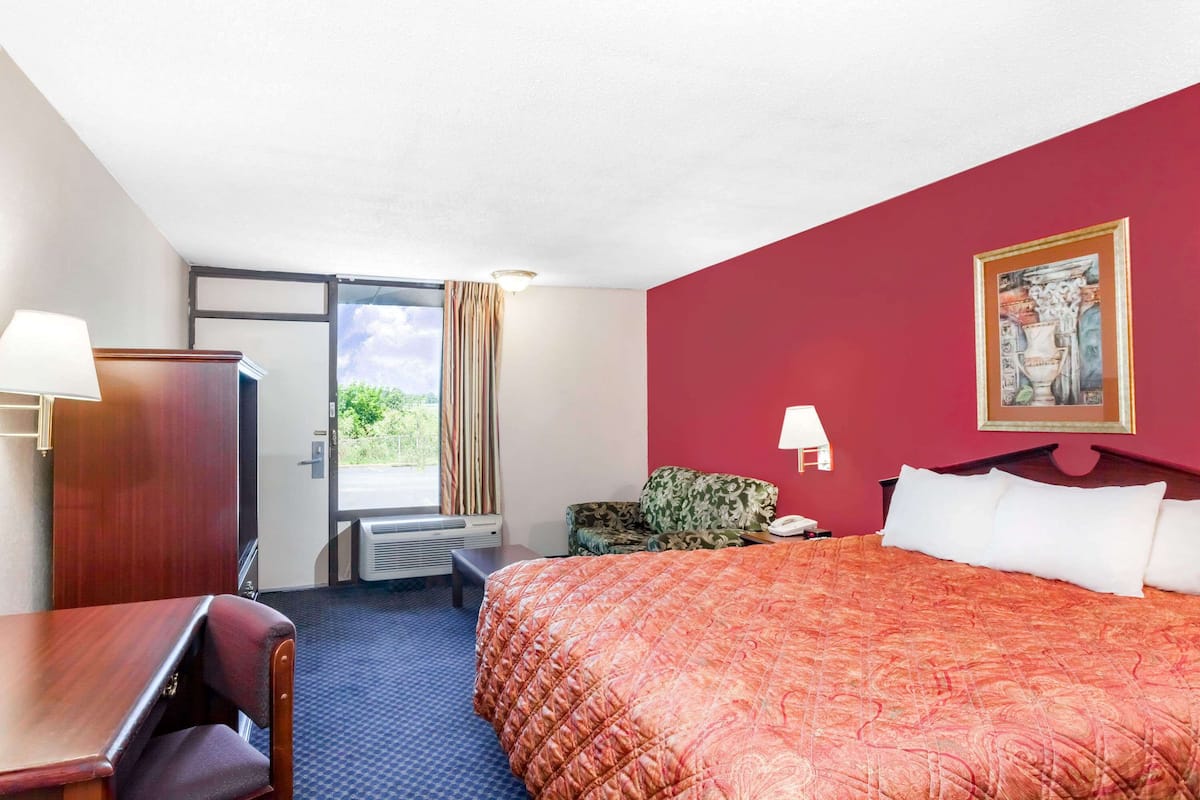 Une chambre d’hôtel avec un lit, un bureau, une chaise, une fenêtre avec des rideaux et une porte.