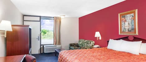 A hotel room with a bed, a desk, a chair, a window with curtains, and a door.