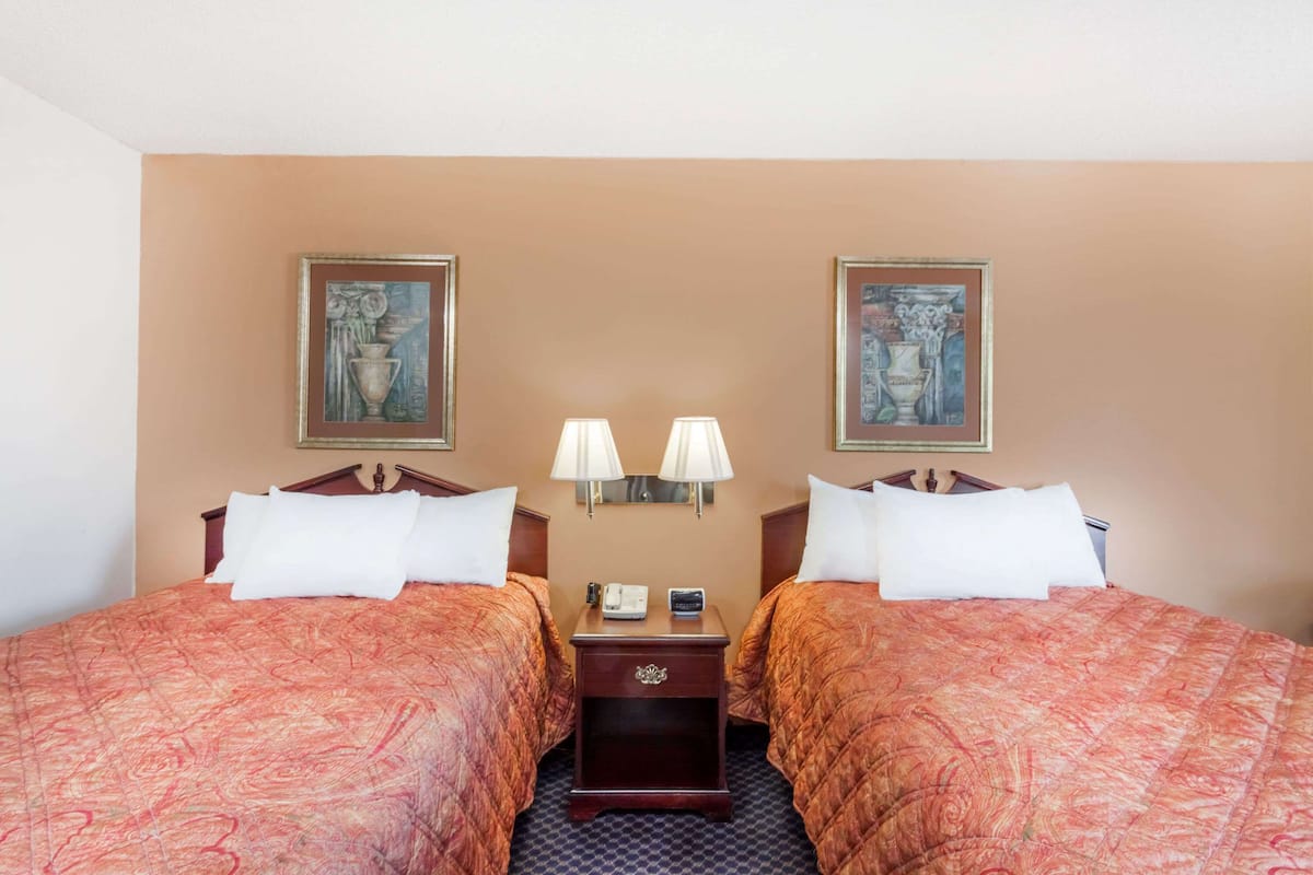 Une chambre d’hôtel avec deux lits, chacun recouvert d’une couvre-lit à motifs rouges, agrémentée de coussins blancs et d’une table de chevet avec une lampe placée entre les deux.