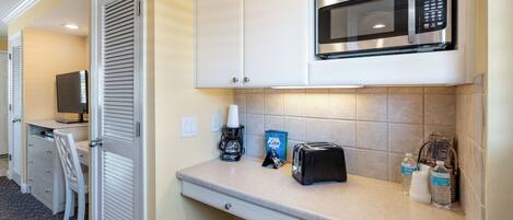 A compact kitchenette with a microwave, toaster, coffee maker, and a trash bin.