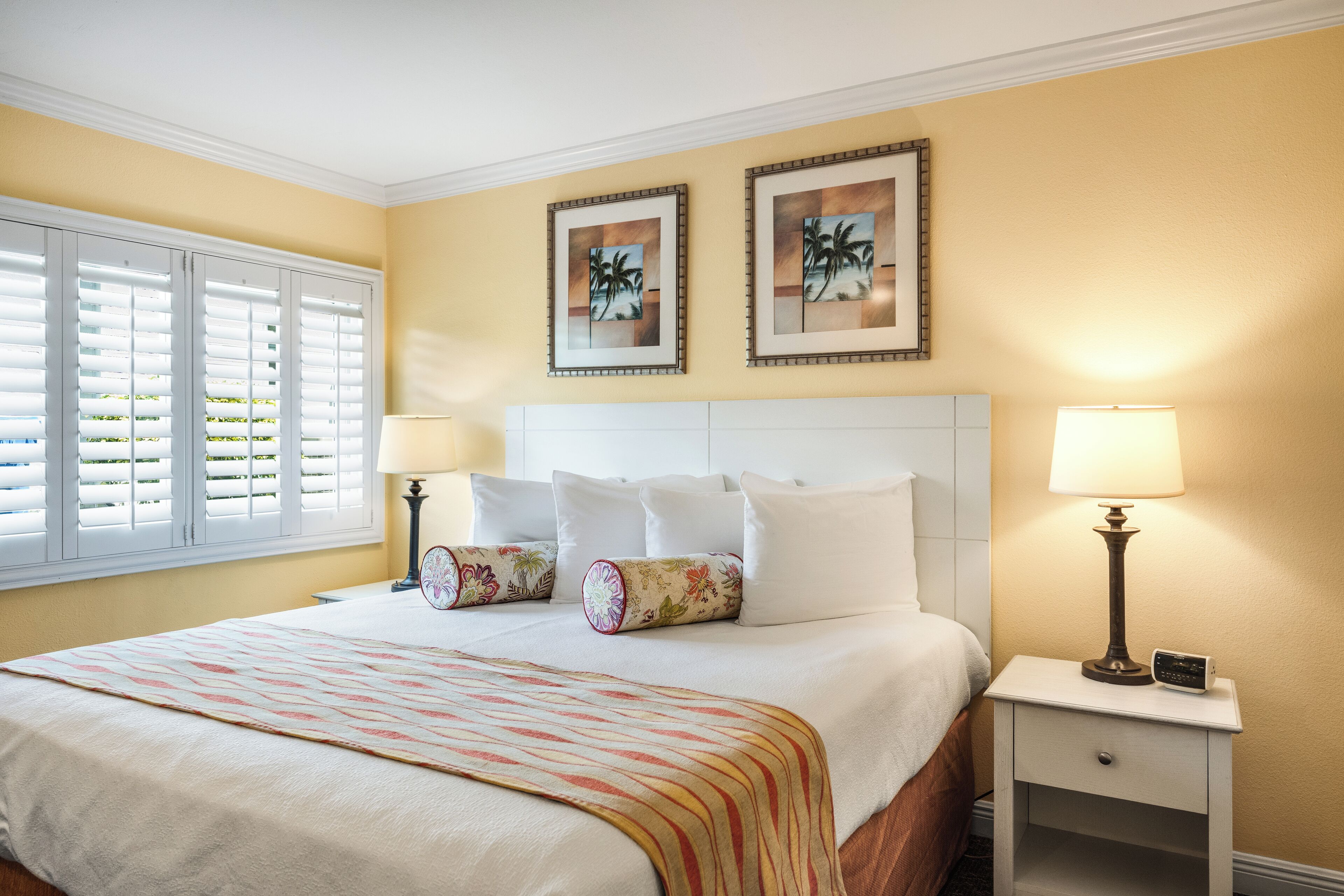 A hotel room with a large bed, two bedside lamps, a nightstand, and two framed pictures on the wall.
