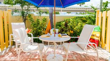 A patio with a round table, four white chairs, and a blue umbrella.