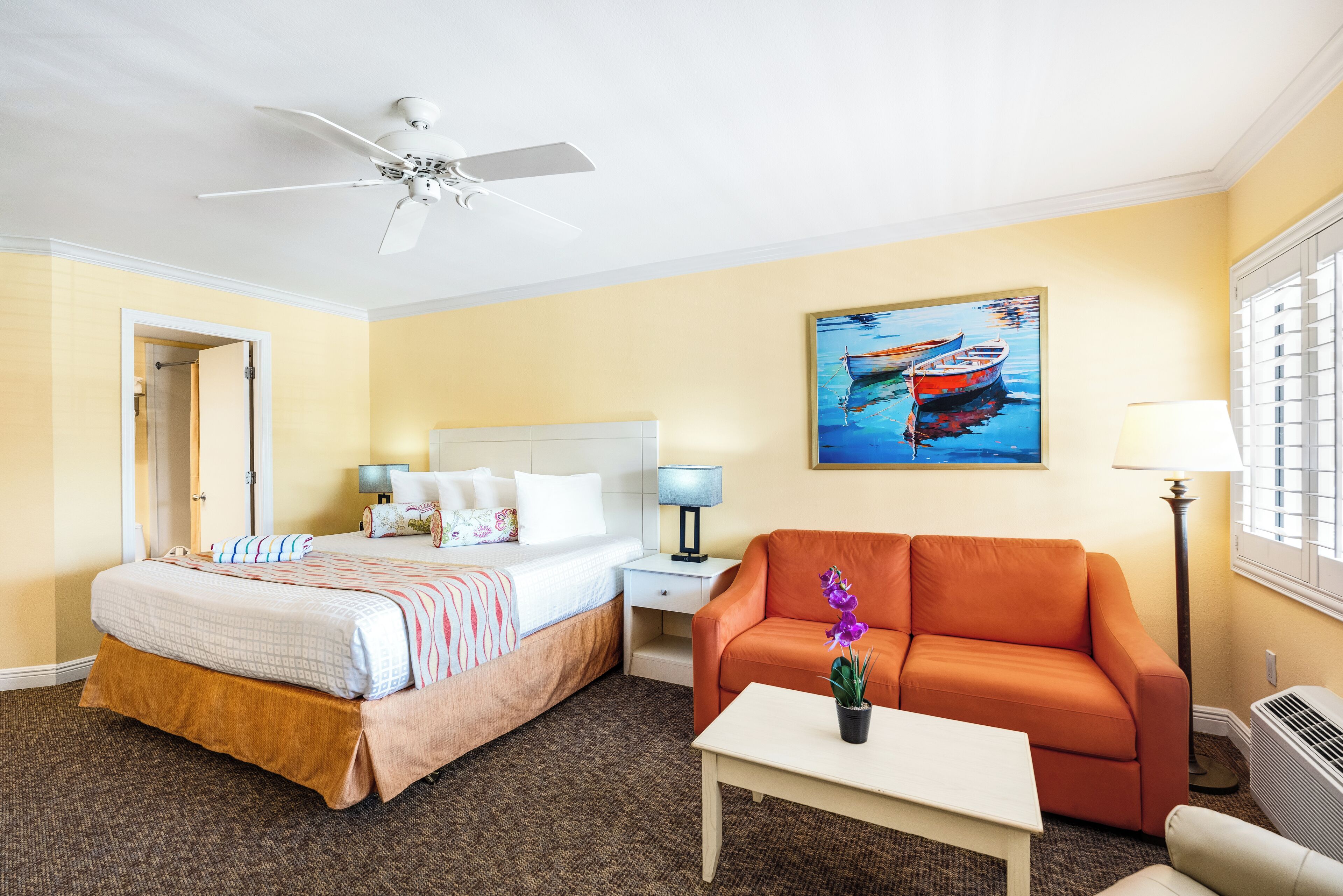 Une chambre d’hôtel avec un lit, un canapé, une table, un tableau et un ventilateur de plafond.