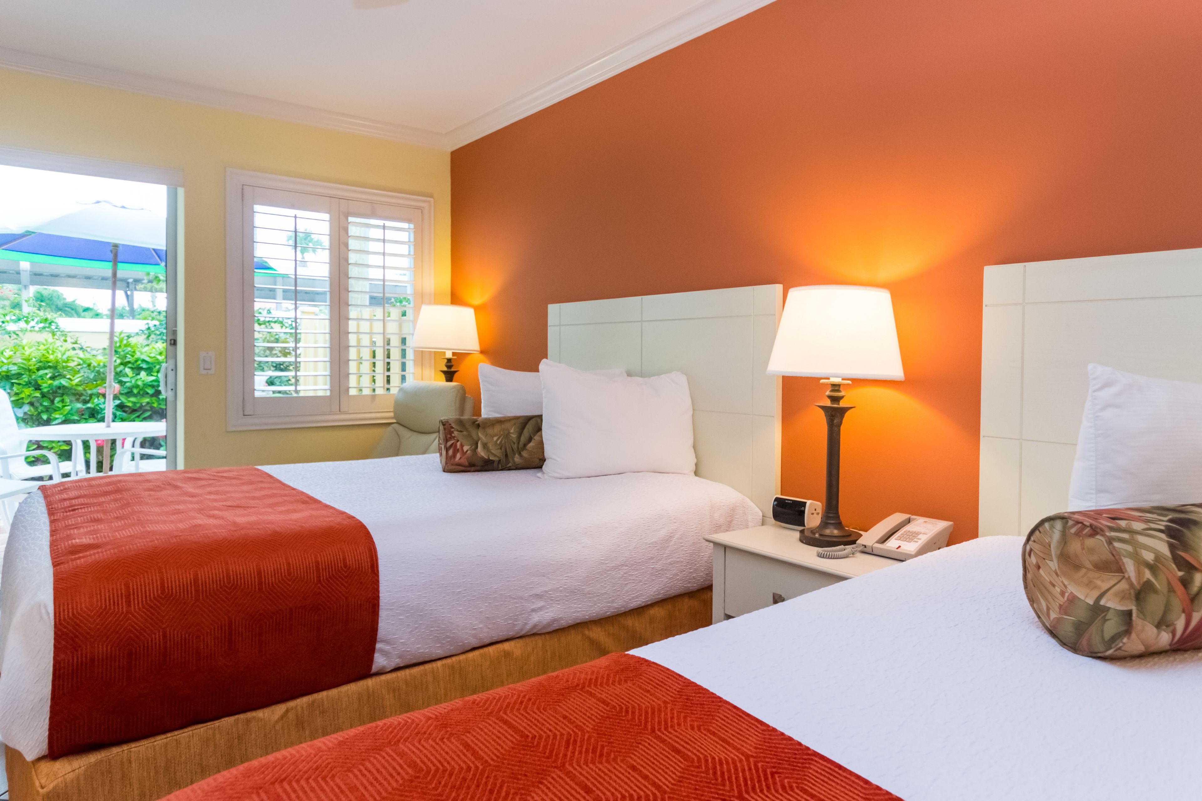 A hotel room with two beds, each with a red and white bedspread, white pillows, and a nightstand with a lamp and phone.
