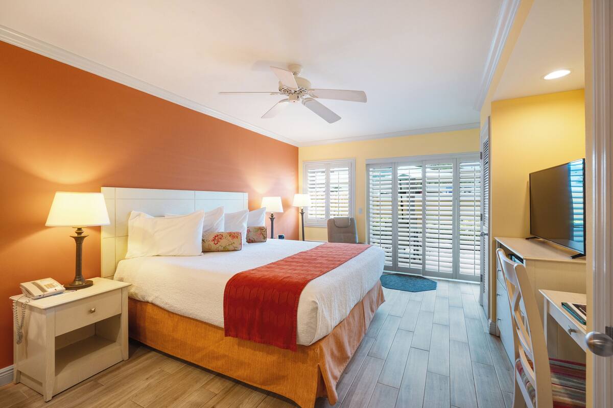 A hotel room with a bed, bedside lamps, a telephone, a ceiling fan, and a television.