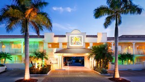 Un hotel con entrada flanqueada por una palmera, un letrero de neón y techo de tejas.