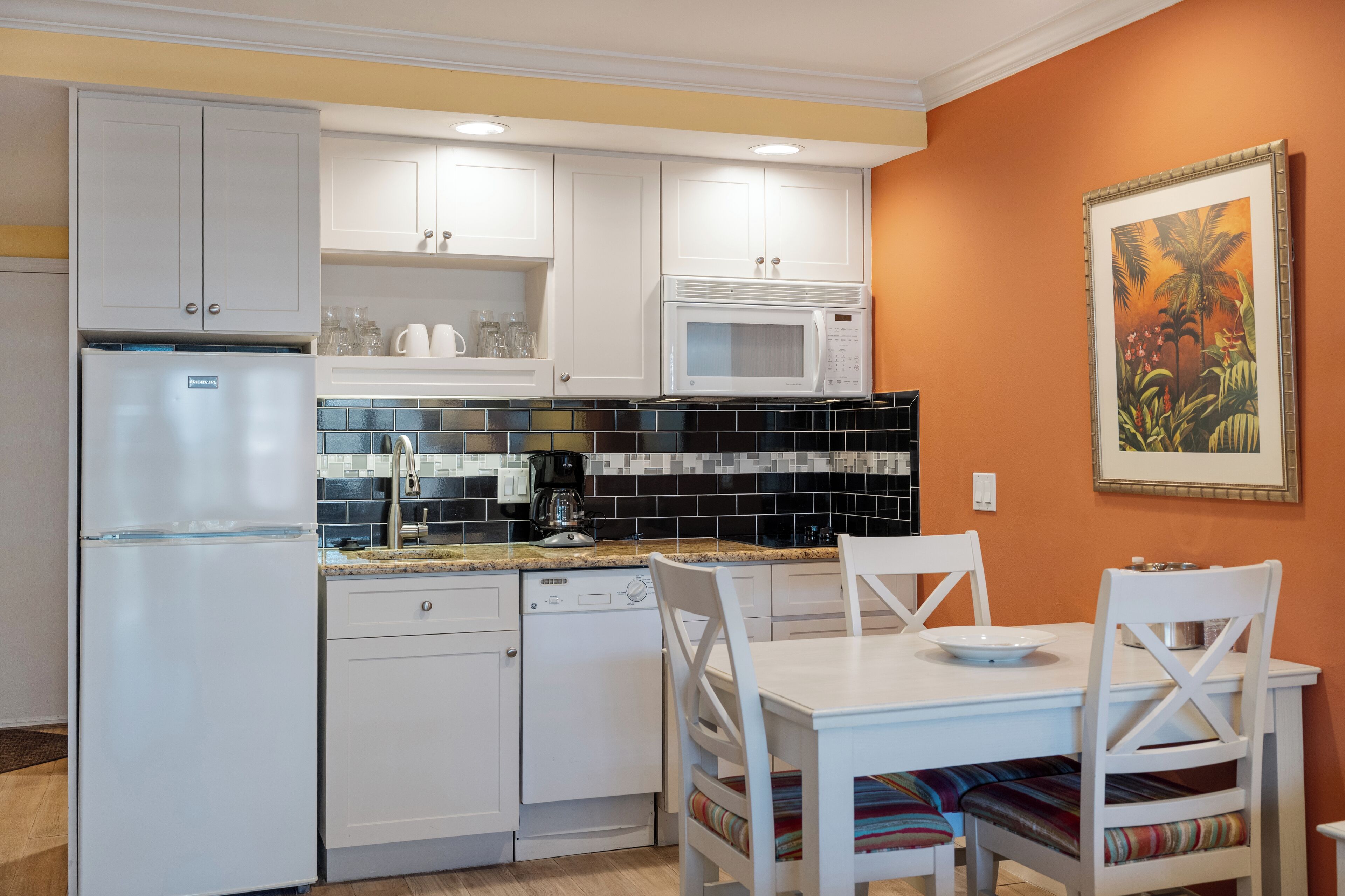 Una cucina compatta con mobili bianchi, un forno a microonde, una lavastoviglie e un'area pranzo con tavolo e sedie bianche.