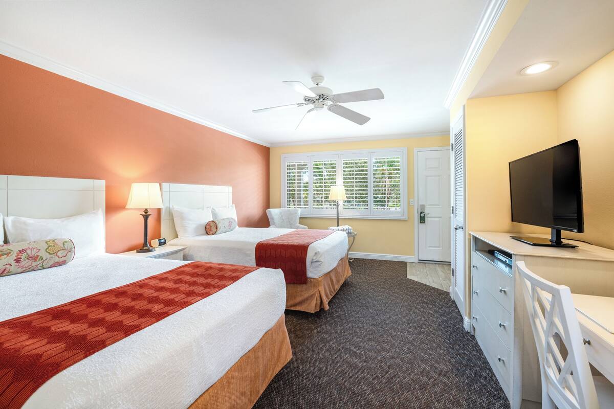 A hotel room with two beds, a TV, a desk, and a ceiling fan.