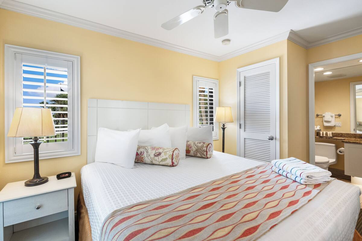 A hotel room with a bed, nightstand, lamp, and a ceiling fan.