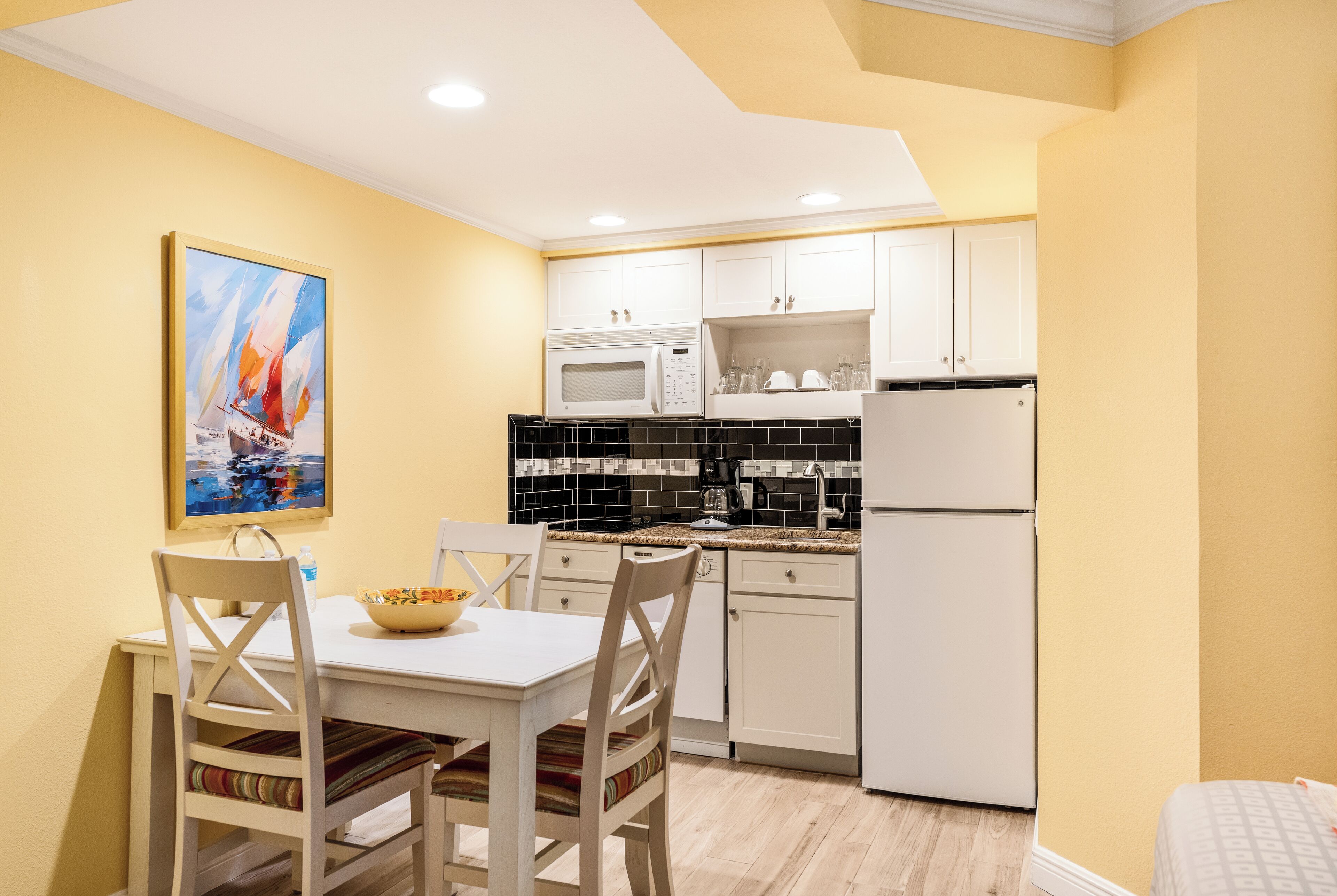 Una cocina compacta con gabinetes blancos, microondas, refrigerador y un comedor con mesa y sillas.