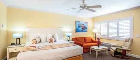 A hotel room with a bed, a sofa, a chair, a desk, and a ceiling fan.