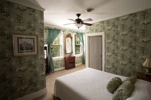 A bedroom with floral wallpaper, a bed with green pillows, a ceiling fan, and a framed picture on the wall. - Maplewood Hotel (Saugatuck)