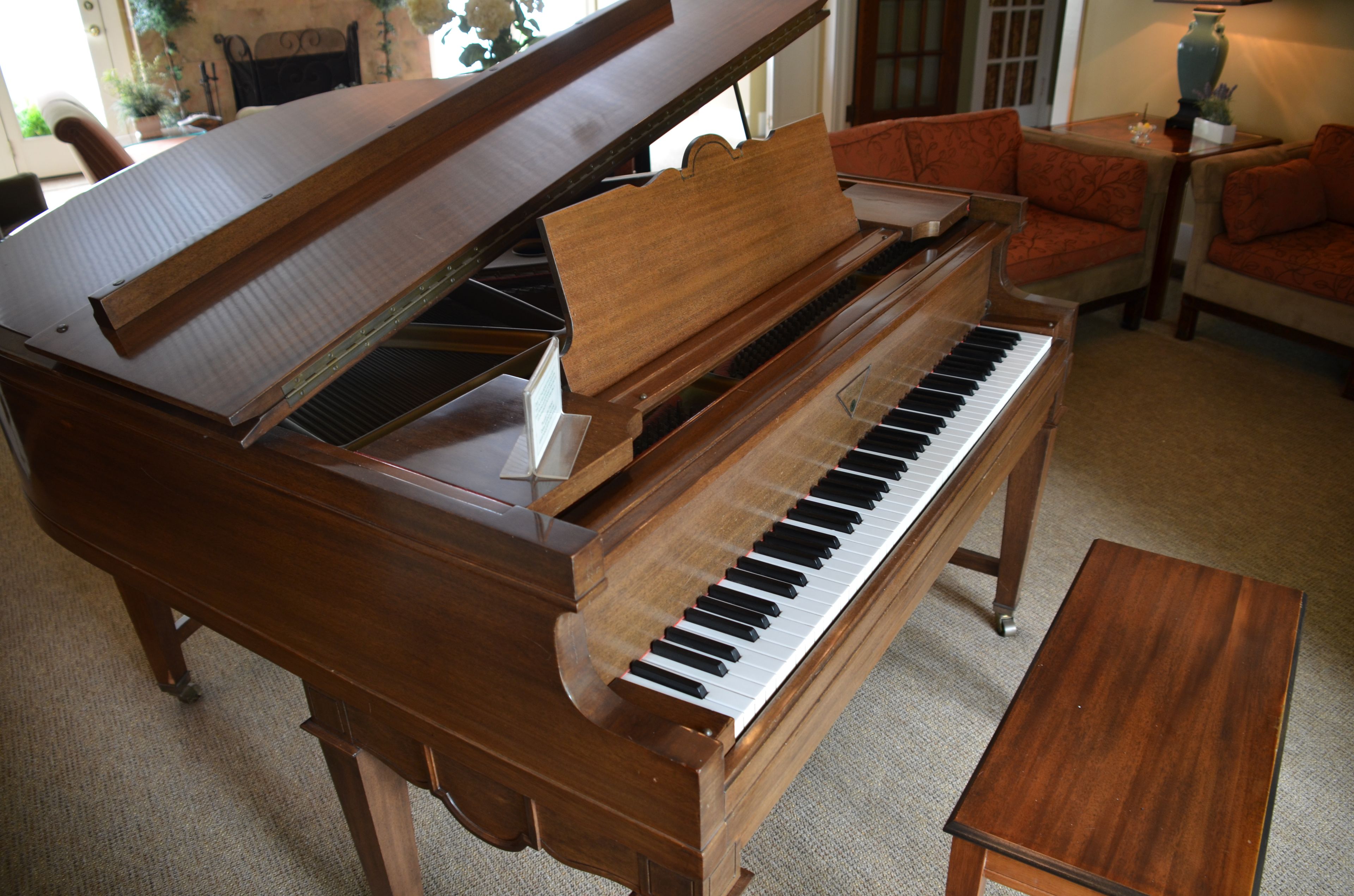 A grand piano in a room with a carpeted floor, a small wooden table, and two upholstered chairs.