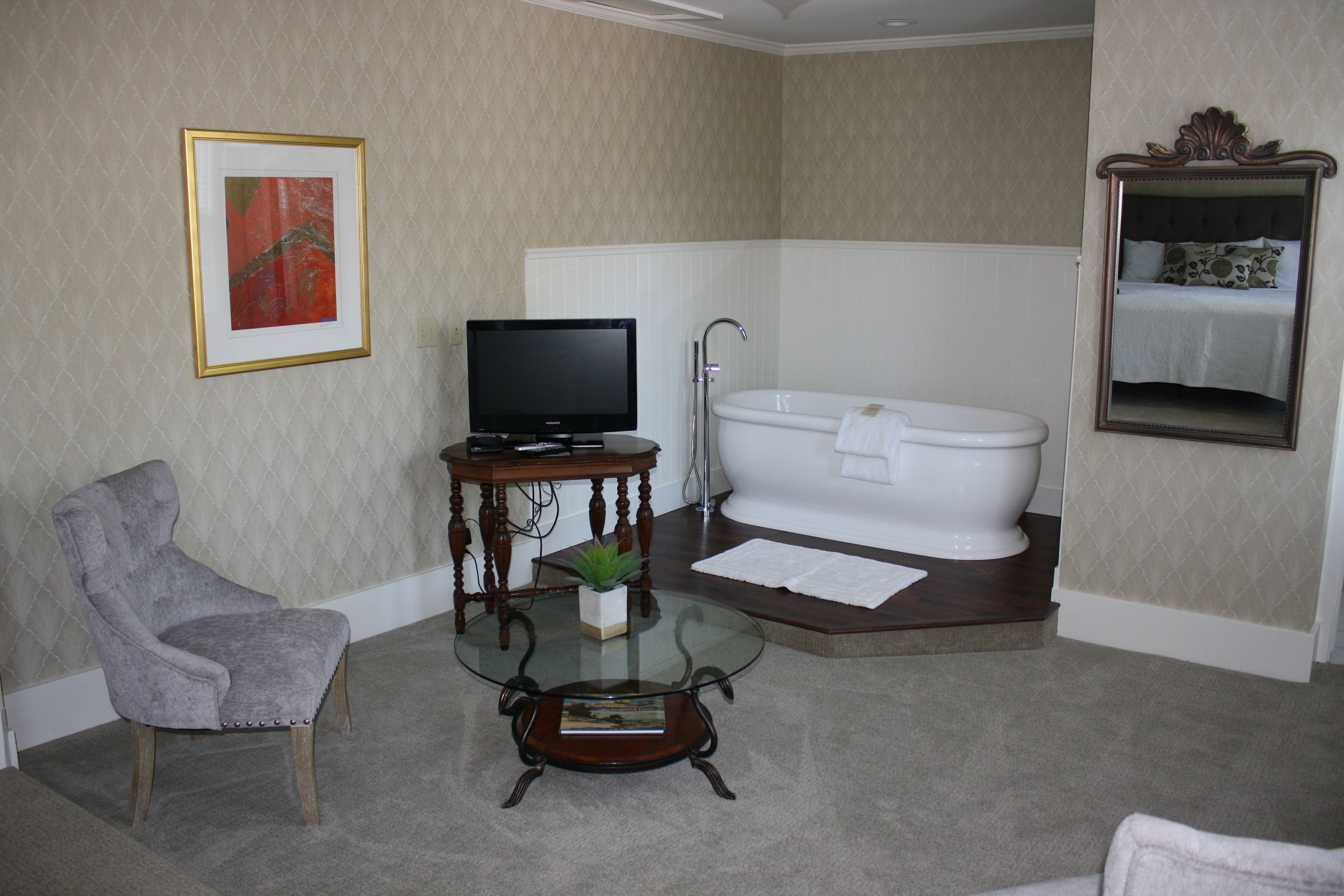 A bathroom with a bathtub, a chair, a television, and a framed picture on the wall.