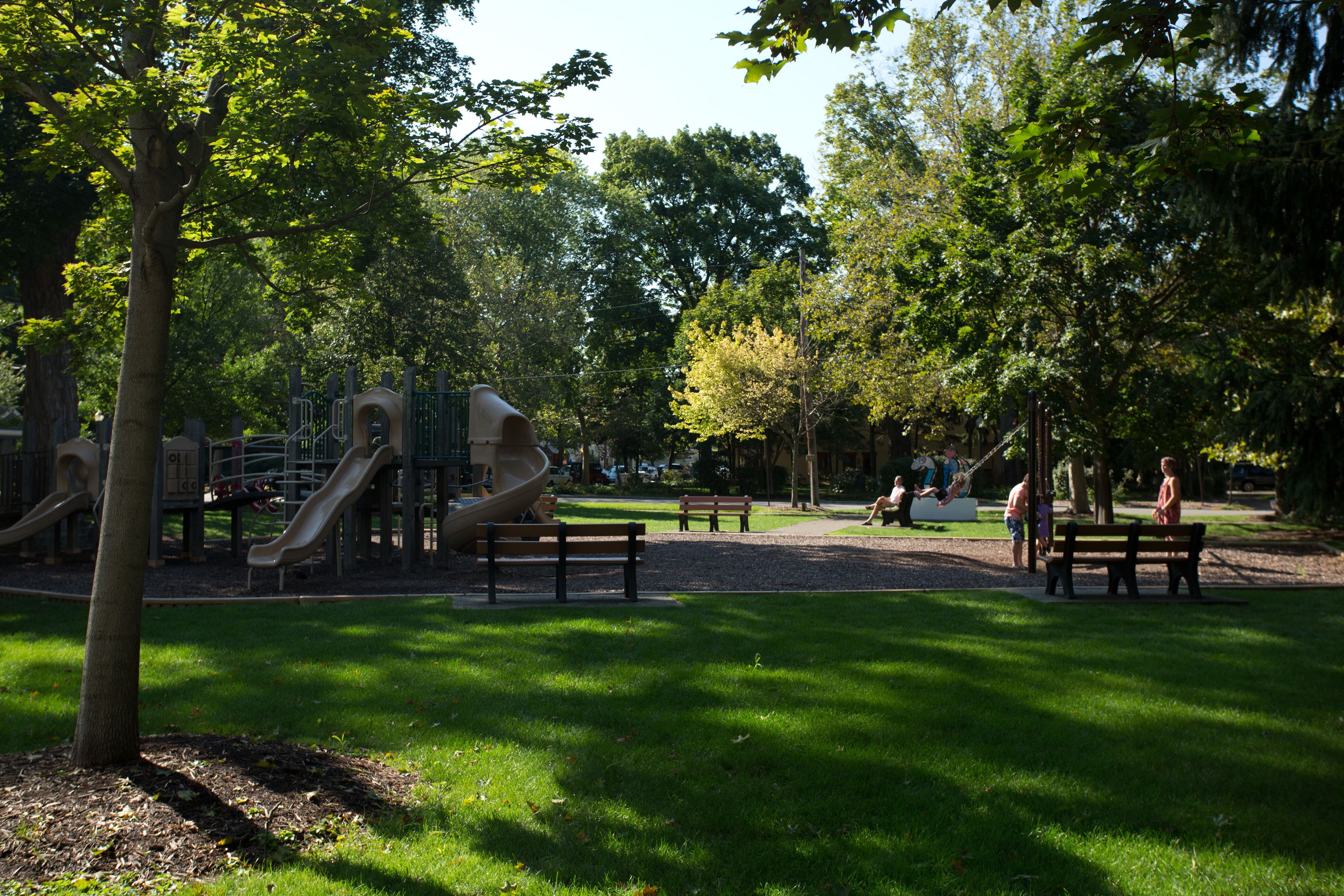 A park with playground equipment, benches, and trees.