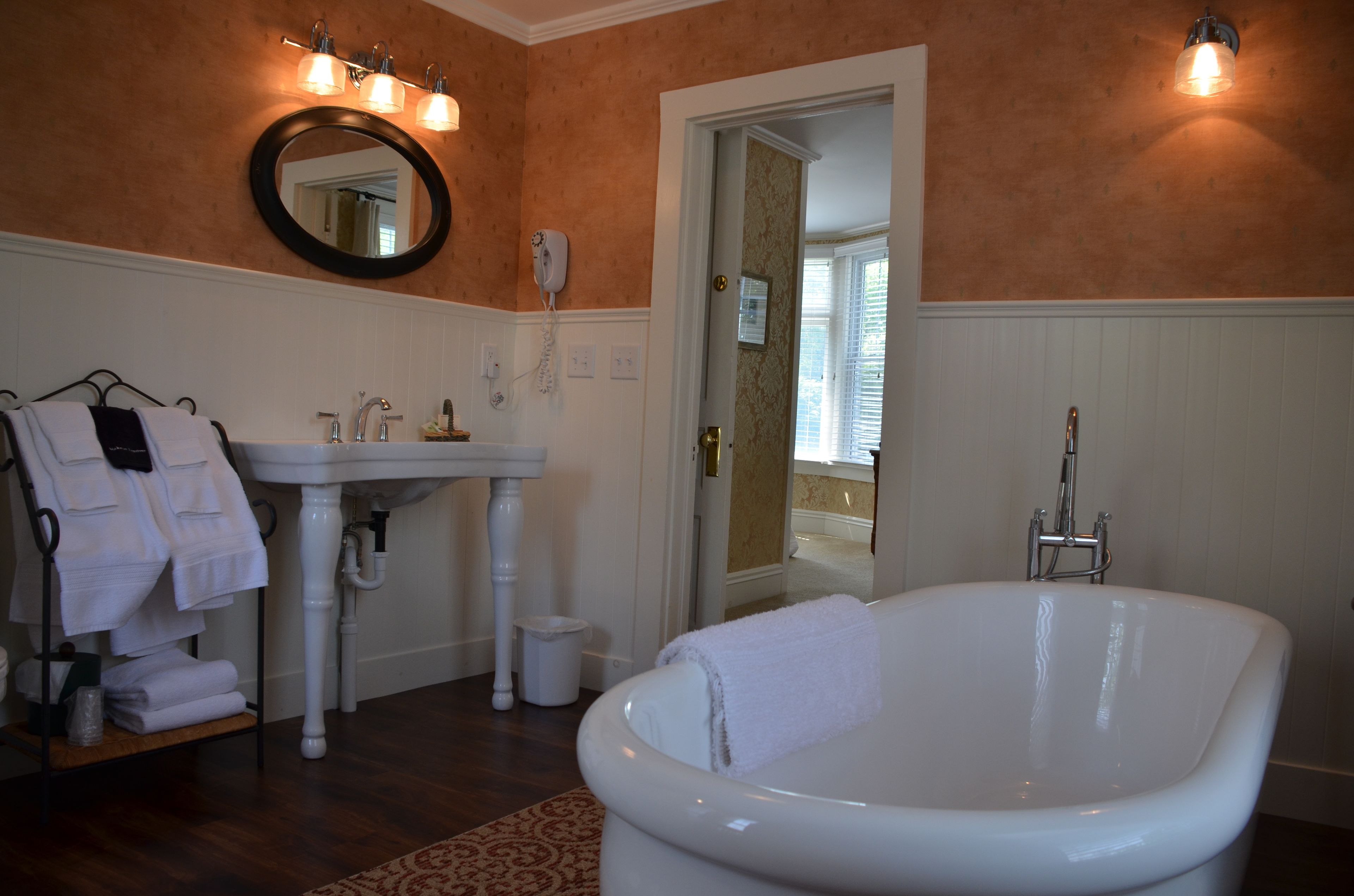 A bathroom with a white sink, a round mirror, a white bathtub, and a towel rack with towels.