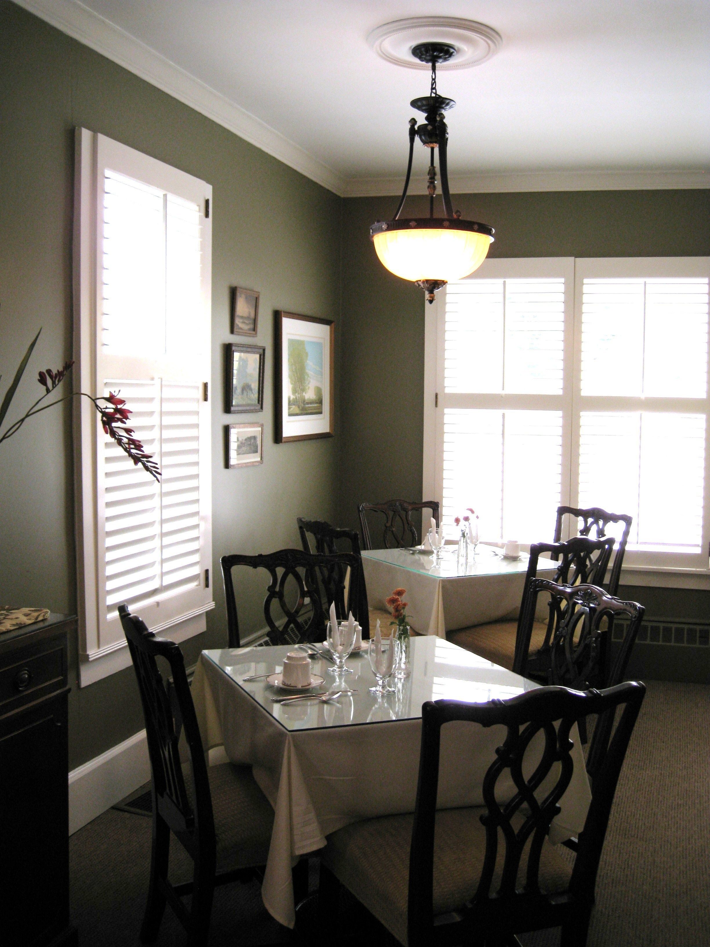 A dining area with a glass table, dark wooden chairs, a chandelier, and framed pictures on the wall.