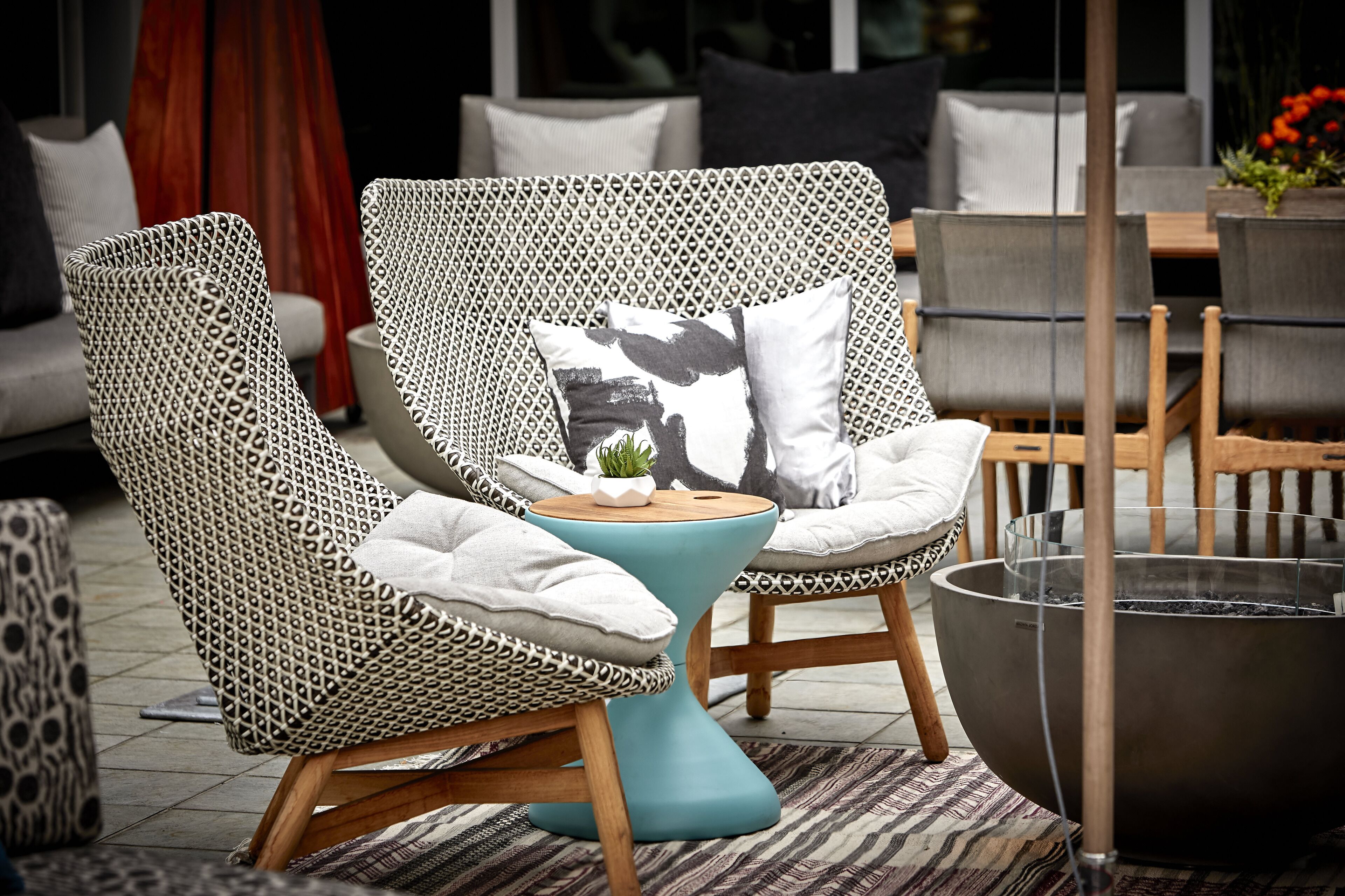 Un fauteuil de jardin en osier avec un coussin, une petite table et un foyer.