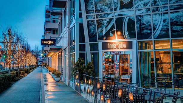 A modern building with a 'hook&pull' sign, outdoor seating, and a pathway lined with trees.