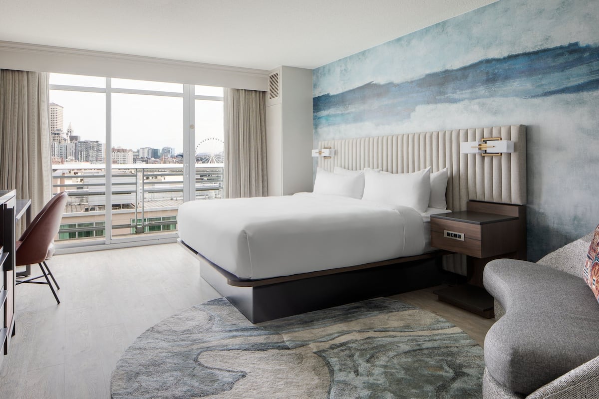 A modern hotel room with a large bed, a desk, and a view of the cityscape.