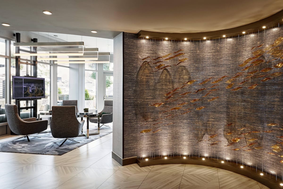 A modern lobby with a curved wall featuring a metallic fish sculpture, contemporary seating, and a large flat-screen TV.