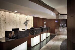A modern reception area with marble reception desks, a wooden wall, and a seating area in the background.